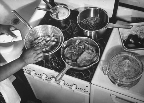 Battle Of The Metals. Woman testing efficiency of pots and pans made of different metals as she cooks various foods including potatoes in an aluminum pot, cutlets in a cast iron skillet, peas in a stainless steel pan and sauce in a copper pot with lid (USA 1939)