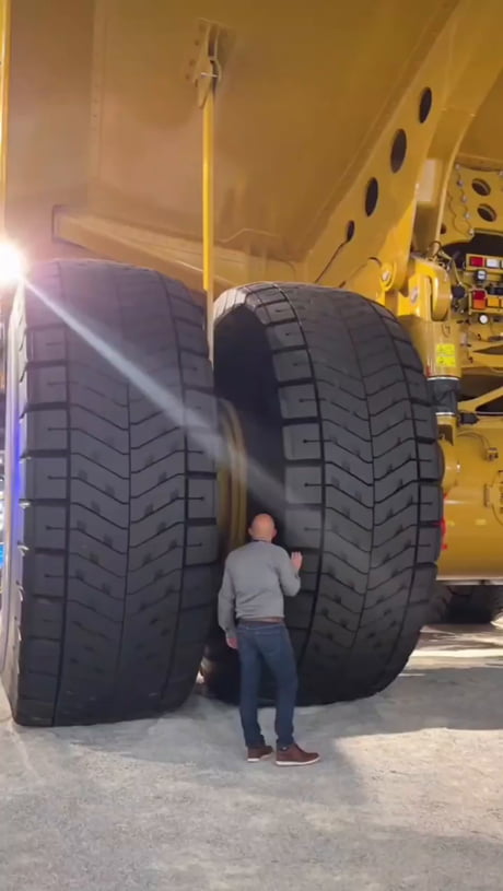 A person walking under a giant mining truck, showing the sheer scale of this industrial beast